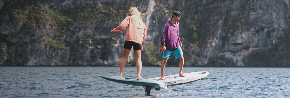 Two riders on Waydoo eFoils beside a rocky coastline